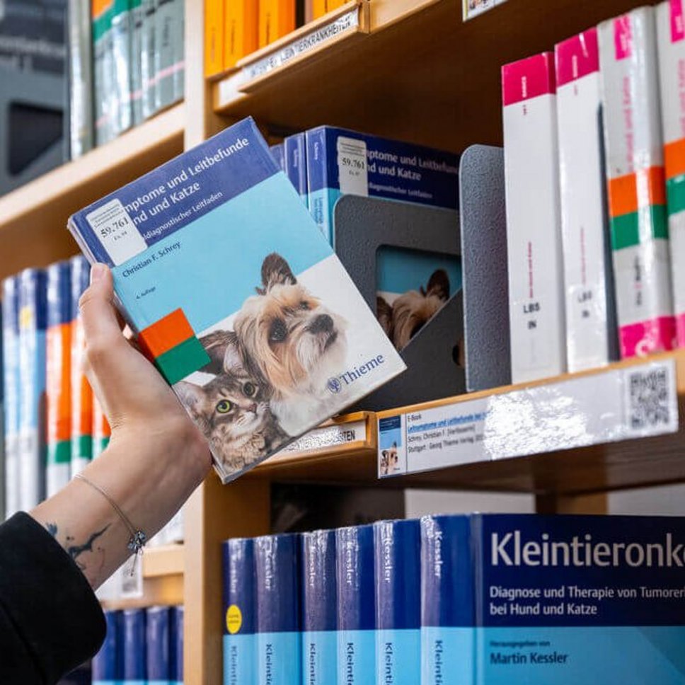 Hand nimmt Buch aus einem Bücherregal der Universitätsbibliothek